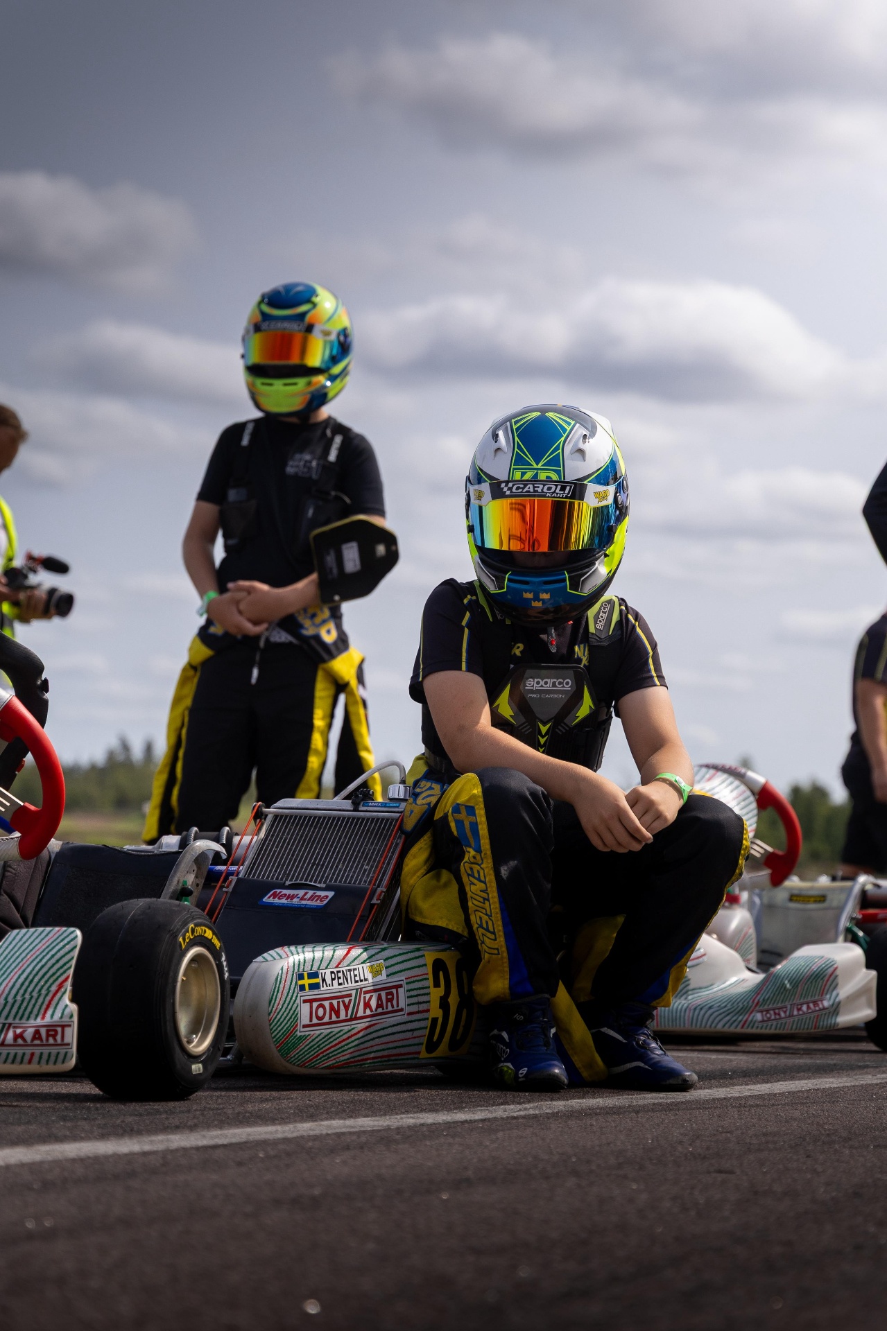Kevin Pentell helmet on, crouched beside the kart on the grid